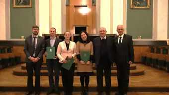 Grupa ludzi z dyplomami w auli elegancko ubrana