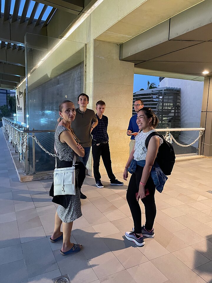 Grupa pięciu osób dyskutuje przed budynkiem