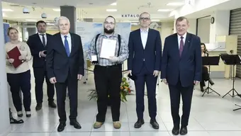 Grupa osób w holu jedna z nich trzyma w ręku dyplom